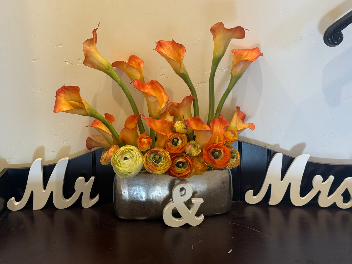 Orange Calla Lily centerpiece rental with orange calla lilies and orange ranunculus in silver metallic vase on dark wood console table with Mr and Mrs sign at indoor home entryway | Reno, Lake Tahoe & Sacramento