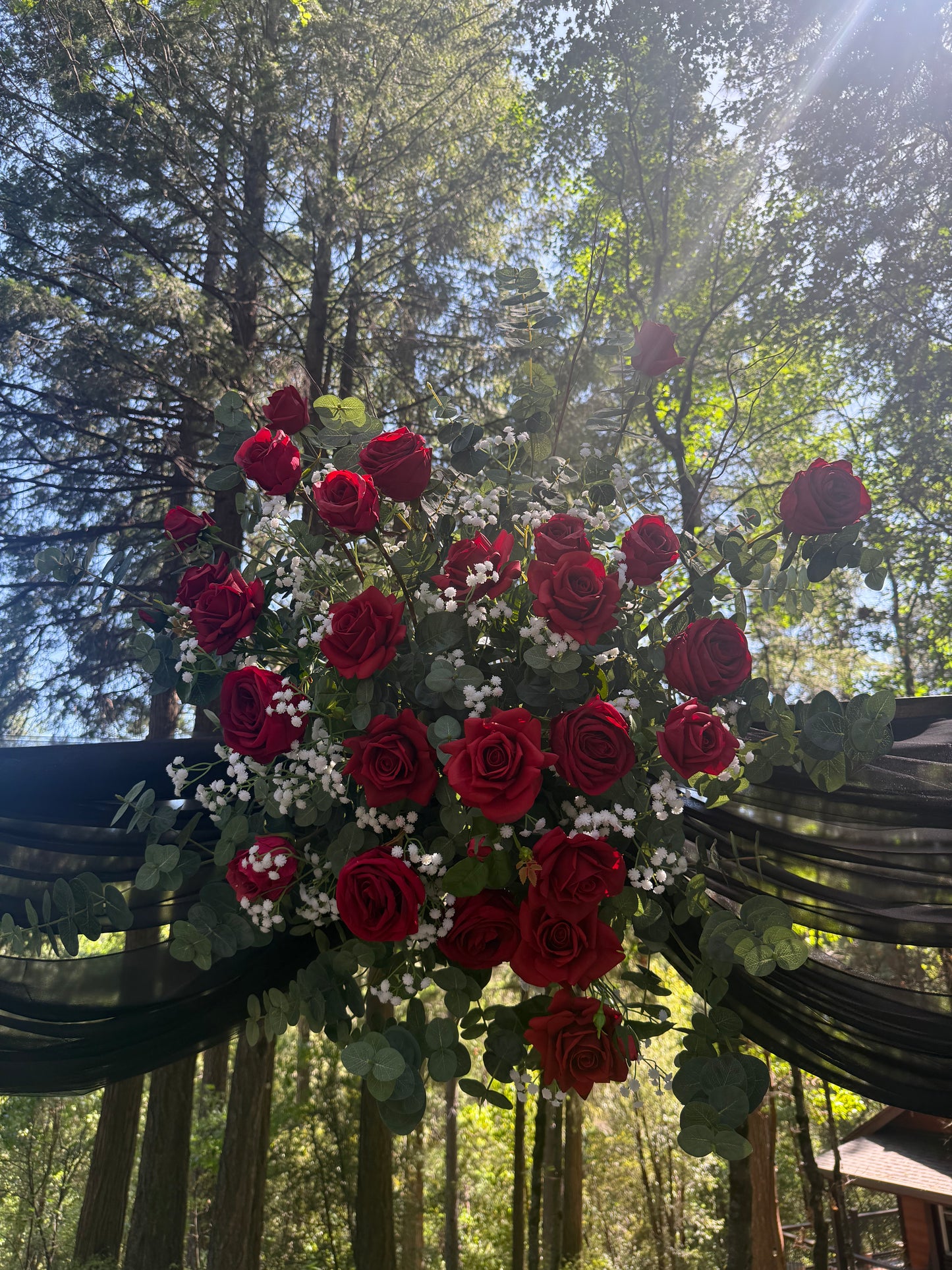 Close-up of red rose and baby's breath arch adornment rental cluster on black drapery at outdoor forest wedding ceremony | Reno, Lake Tahoe & Sacramento