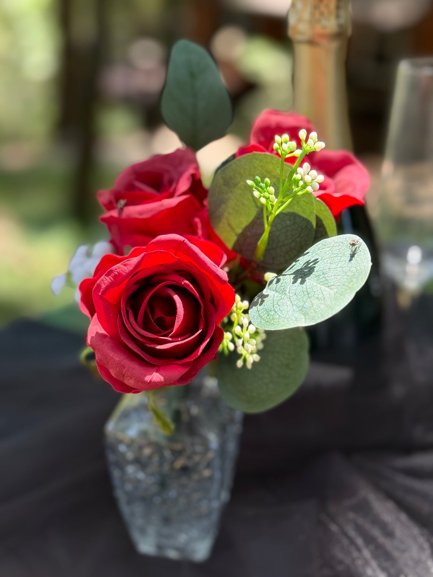 Red rose centerpiece rental with bold red roses, baby's breath, and eucalyptus in glass bud vase at outdoor forest wedding with black drapery | Reno, Lake Tahoe & Sacramento