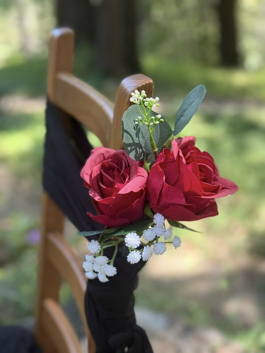 Close-up of red rose aisle chair flower rental with baby's breath and eucalyptus tied to cross-back chair with black fabric tie at outdoor pine forest wedding venue | Reno, Lake Tahoe & Sacramento