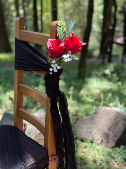 Red rose aisle chair flower rental with baby's breath and eucalyptus tied with long black fabric tie on cross-back chair at outdoor pine forest wedding venue | Reno, Lake Tahoe & Sacramento