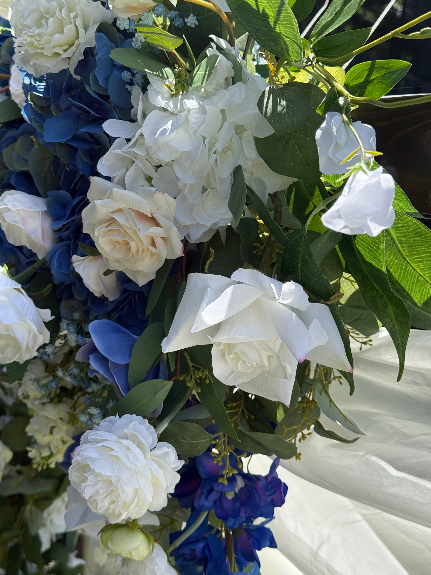 Close-up of Sweet Nothings arch adornment rental with white garden roses, blue hydrangea, and navy delphinium with white drapery in bright sunlight | Reno, Lake Tahoe & Sacramento
