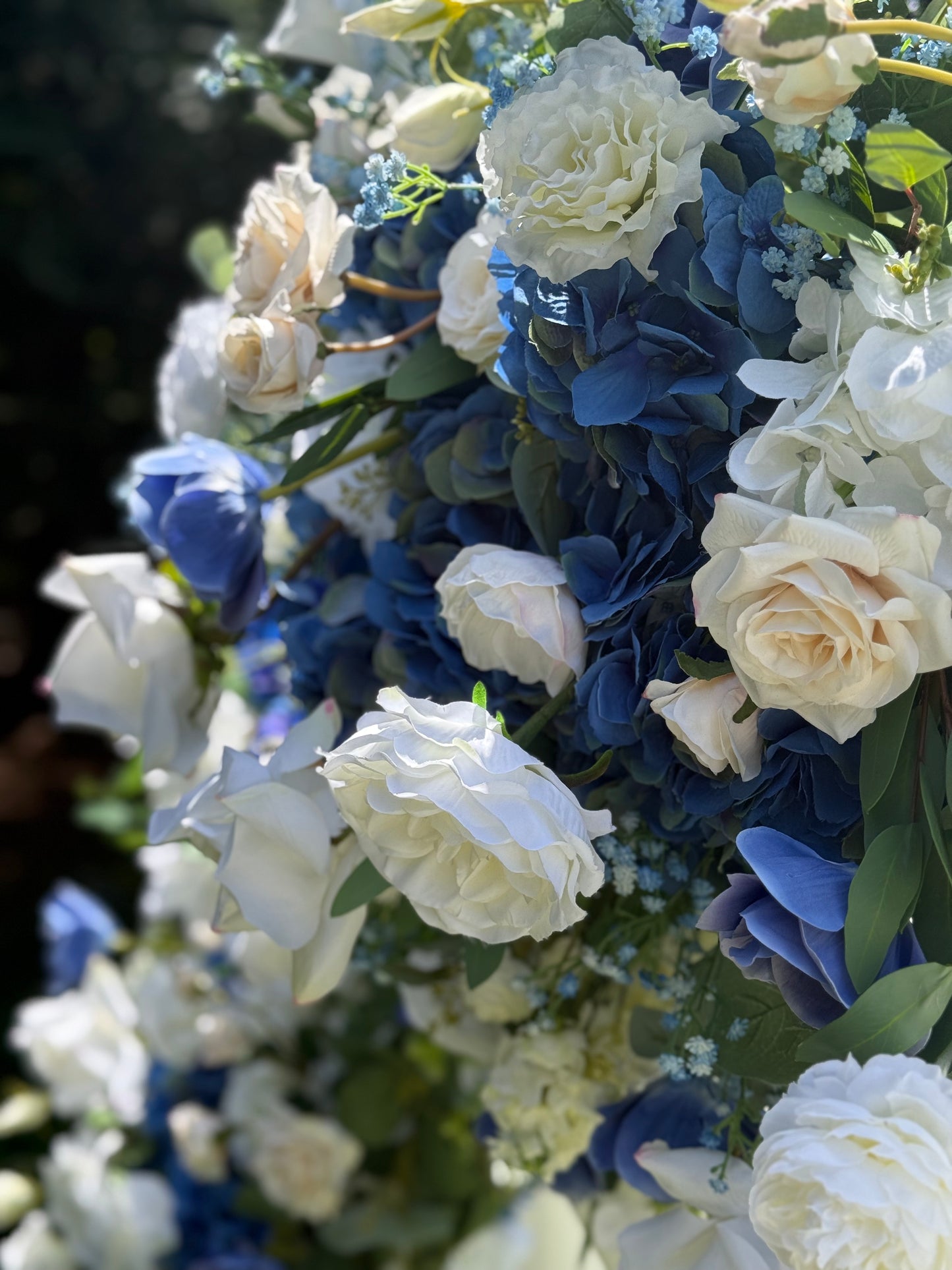 Close-up of Sweet Nothings arch adornment rental with white garden roses, blue hydrangea, and navy delphinium with white drapery in bright sunlight | Reno, Lake Tahoe & Sacramento