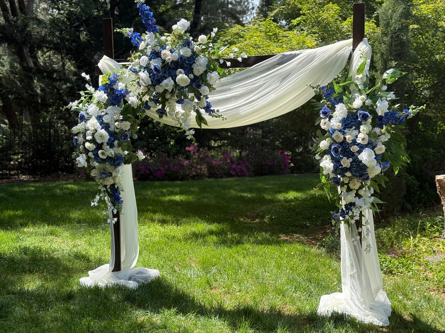 Full Sweet Nothings arch adornment rental with navy blue delphinium, white roses, blue hydrangea, and white drapery on rustic wood arch at outdoor garden wedding | Reno, Lake Tahoe & Sacramento