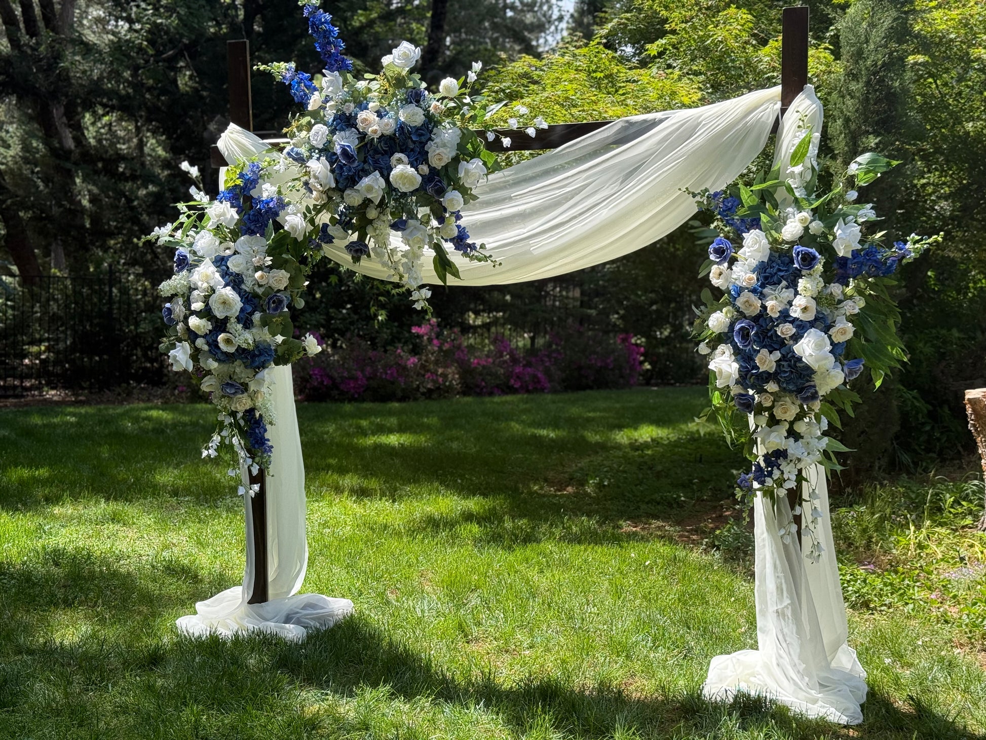 Full Sweet Nothings arch adornment rental with navy blue delphinium, white roses, blue hydrangea, and white drapery on rustic wood arch at outdoor garden wedding | Reno, Lake Tahoe & Sacramento