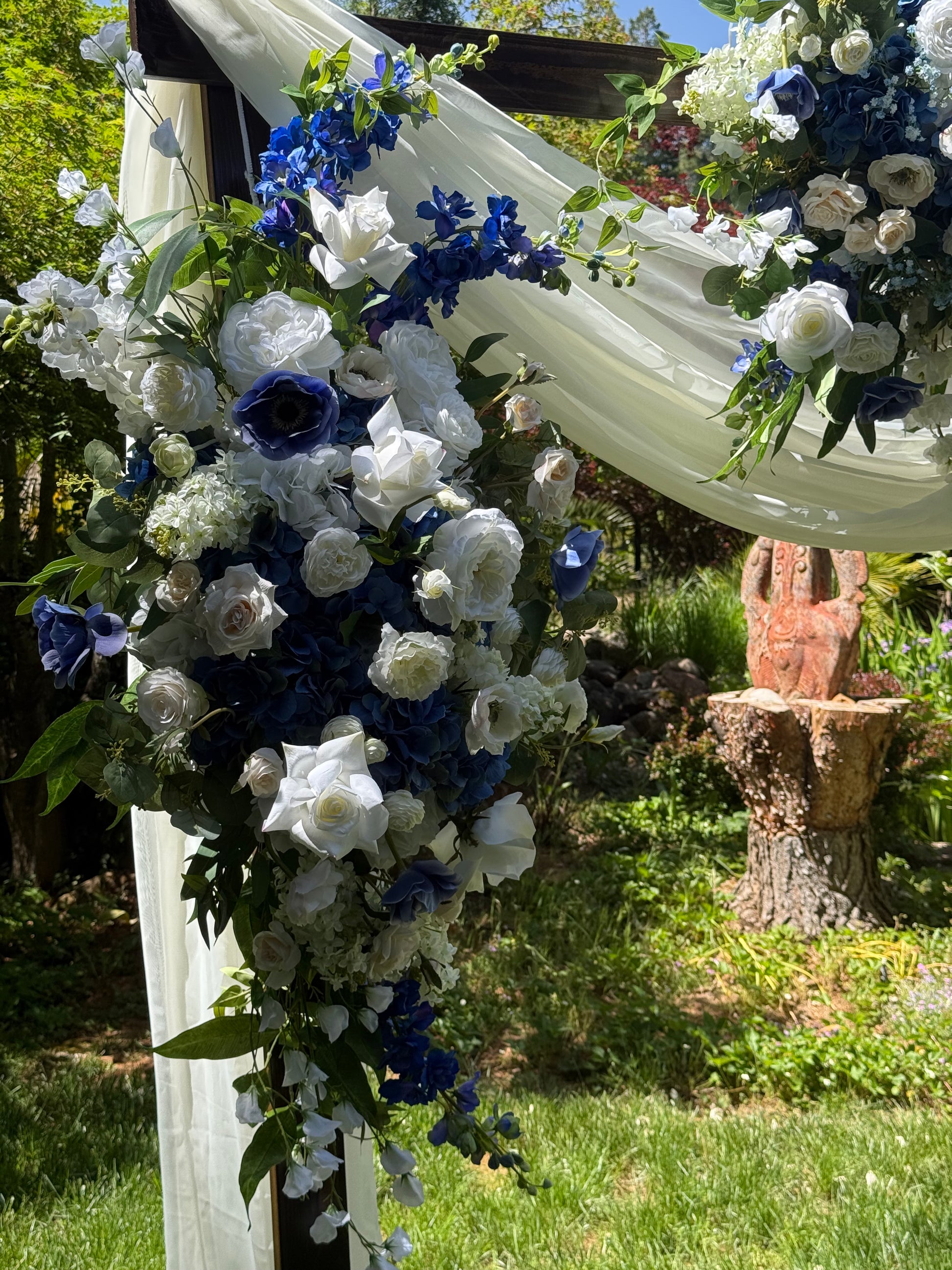 Side view of Sweet Nothings arch adornment rental with navy blue delphinium, white roses, blue hydrangea, and white drapery on rustic wood arch at outdoor garden wedding | Reno, Lake Tahoe & Sacramento