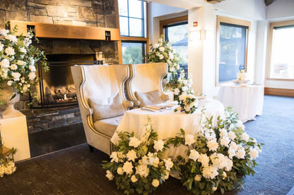 Enchanted aisle flower rentals styled at sweetheart table as ground florals with white roses, white hydrangea, and lush greenery surrounding Bride and Groom chairs at indoor Lake Tahoe wedding reception with stone fireplace | Reno, Lake Tahoe & Sacramento