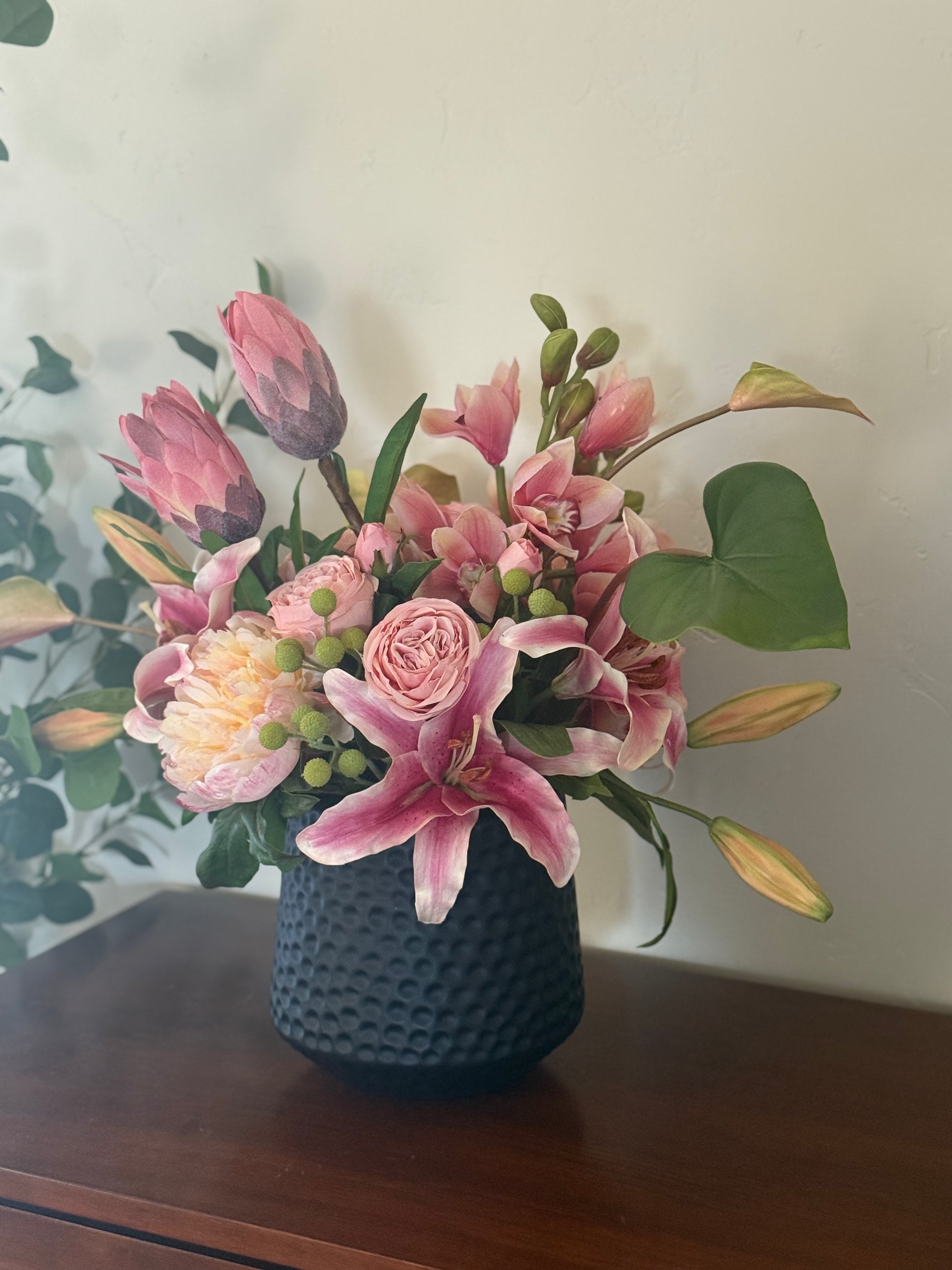 Tropical Blush centerpiece rental with pink stargazer lilies, blush protea, peach garden roses, blush peonies, and hypericum berries in textured black vase styled in bridal suite on wood dresser | Reno, Lake Tahoe & Sacramento