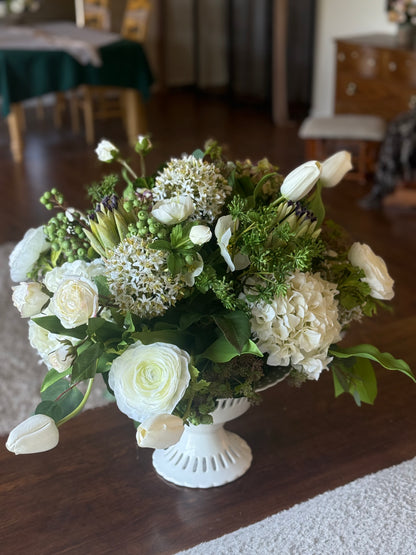 White Garden centerpiece rental with white ranunculus, white hydrangea, white tulips, artichoke blooms, scabiosa, hypericum berries, and lush greenery in white lattice compote vase on wood dining table at indoor wedding reception venue | Reno, Lake Tahoe & Sacramento