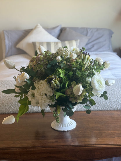 White Garden centerpiece rental with white ranunculus, white hydrangea, white tulips, artichoke blooms, scabiosa, and lush greenery in white lattice compote vase on wood side table at indoor home setting | Reno, Lake Tahoe & Sacramento