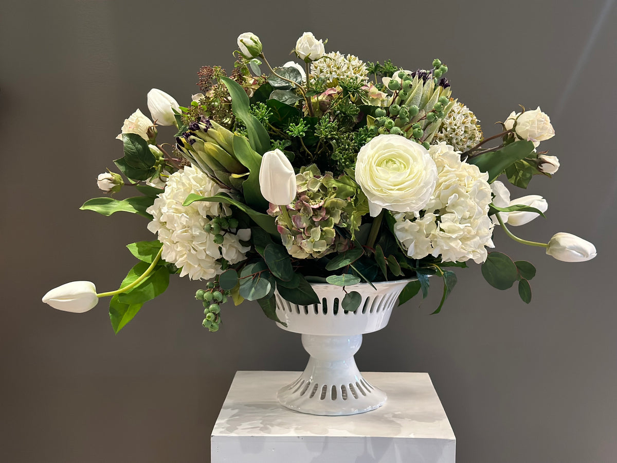 White Garden centerpiece rental with white ranunculus, white hydrangea, white tulips, artichoke blooms, scabiosa, hypericum berries, and lush greenery in white lattice compote vase on white pedestal | Reno, Lake Tahoe & Sacramento
