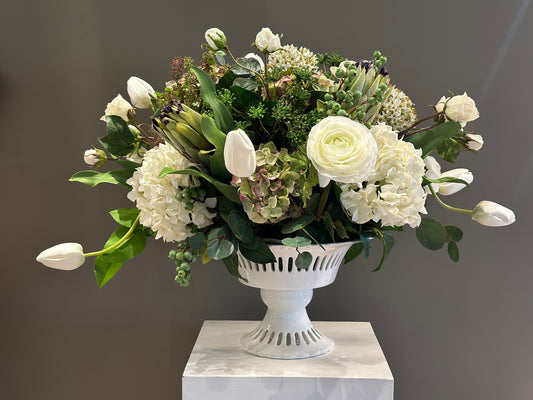 White Garden centerpiece rental with white ranunculus, white hydrangea, white tulips, artichoke blooms, scabiosa, hypericum berries, and lush greenery in white lattice compote vase on white pedestal | Reno, Lake Tahoe & Sacramento