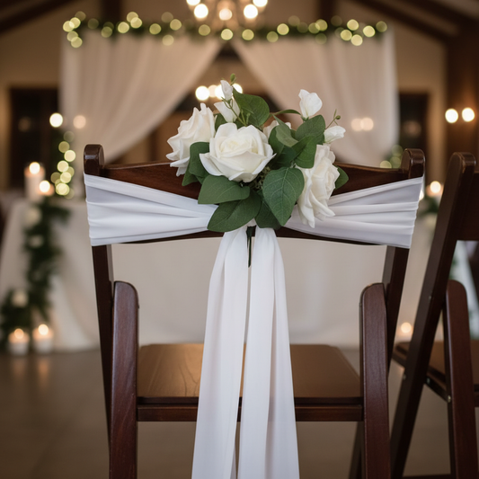 Close-up of White Rose Aisle Chair Flower Rental with white rose cluster and lush green leaves tied with flowing white chiffon ribbon on dark wood folding wedding chair at elegant indoor venue | Reno, Lake Tahoe & Sacramento