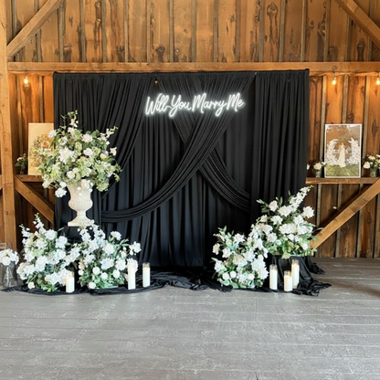 Light-Up LED "Will You Marry Me?" Sign Rental on flowing black spandex drapery backdrop with large Enchanted urn and aisle flower arrangement, and white pillar candles in rustic barn venue with warm wood walls and exposed timber beams | Reno, Lake Tahoe & Sacramento