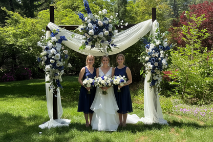 Bride and two bridesmaids posing under Sweet Nothings arch adornment rental with navy blue delphinium, white roses, and white drapery at outdoor garden wedding | Reno, Lake Tahoe & Sacramento