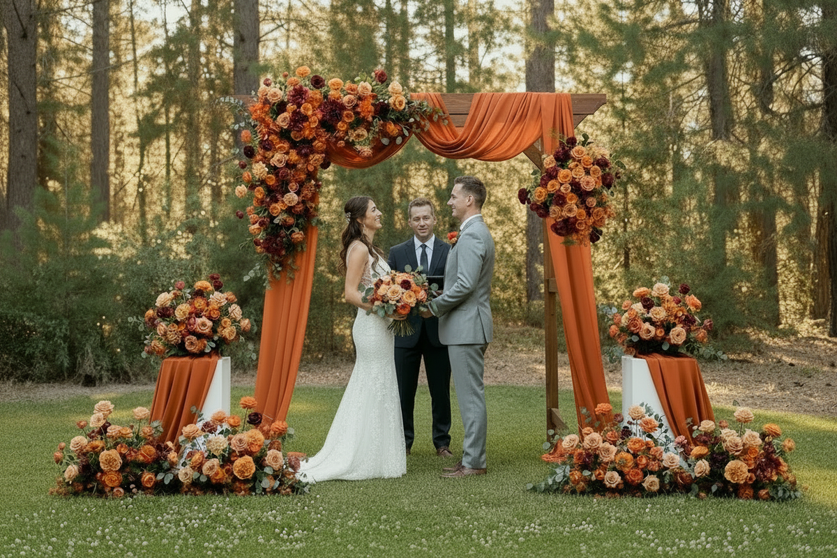 Bride with small bouquet standing under Evermore Fall arch adornment rental with coral, burnt orange, and burgundy florals and rust chiffon drapery | Reno, Lake Tahoe & Sacramento