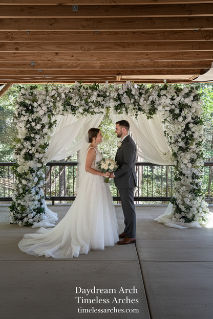 Couple exchanging vows under Daydream arch rental with white roses, hydrangea, and lush greenery at outdoor redwood forest wedding venue | Reno, Lake Tahoe & Sacramento