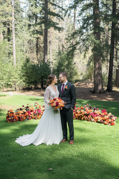 Couple walking through Evermore Fall aisle flower rentals with coral, peach, and burgundy florals lining ceremony aisle at outdoor garden wedding venue | Reno, Lake Tahoe & Sacramento