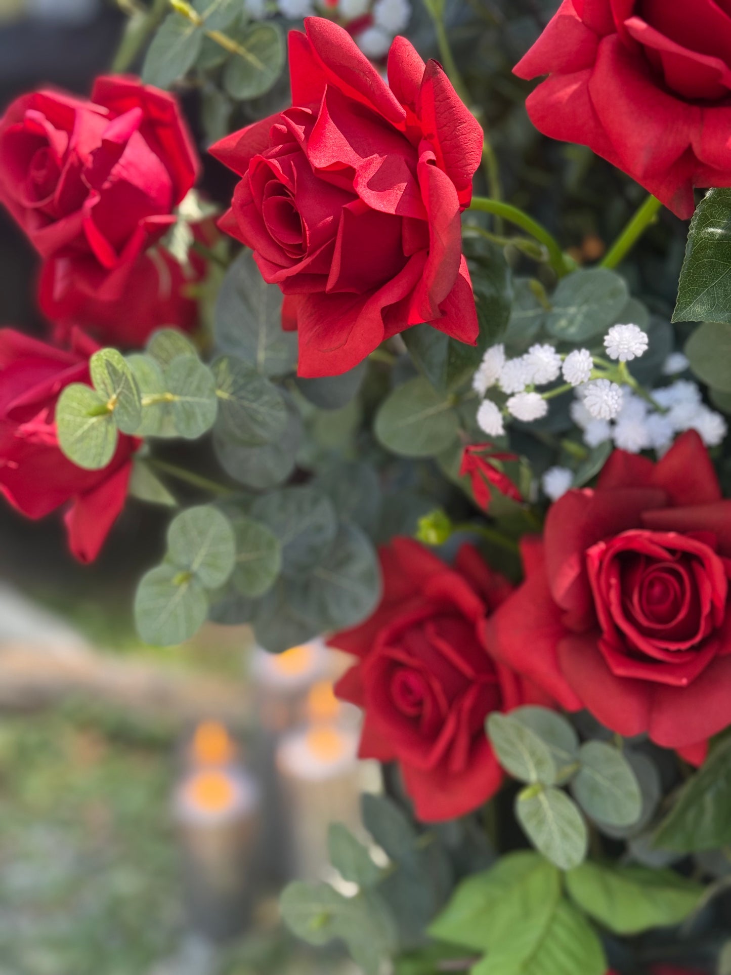 Close-up of bold red roses and eucalyptus in black urn rental with candles glowing in background at outdoor wedding | Reno, Lake Tahoe & Sacramento