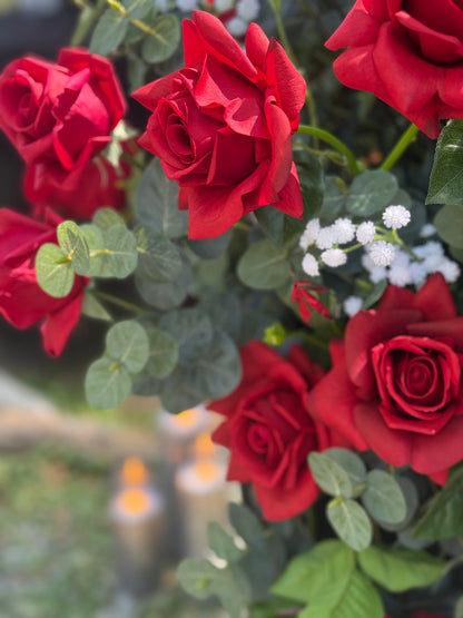 Close-up of bold red roses and eucalyptus in black urn rental with candles glowing in background at outdoor wedding | Reno, Lake Tahoe & Sacramento